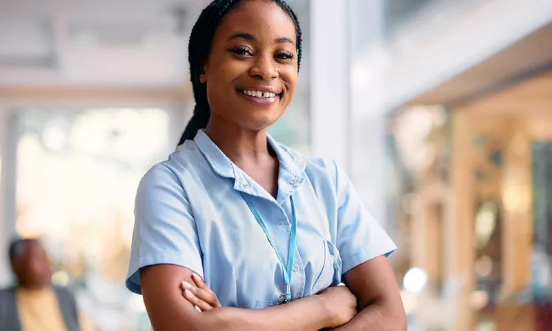 A woman in scrubs smiles while crossing her arms